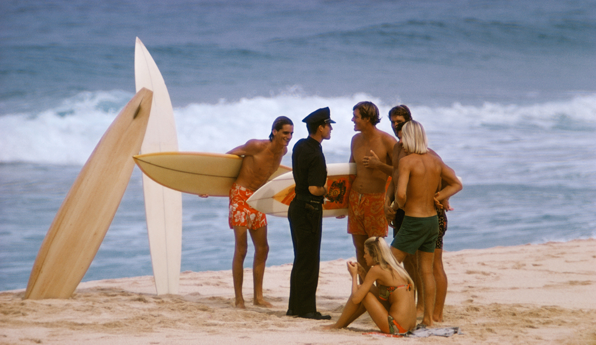 Larry Strada “Wolfman”, Bob Stay, Sherry Haley Juan Shelton and Joey Cabell at Pipeline talking with Hawaii 5-0,  1969. Image: <a href=\"http://www.artbrewer.com/\" target=\"_blank\">Brewer</a>