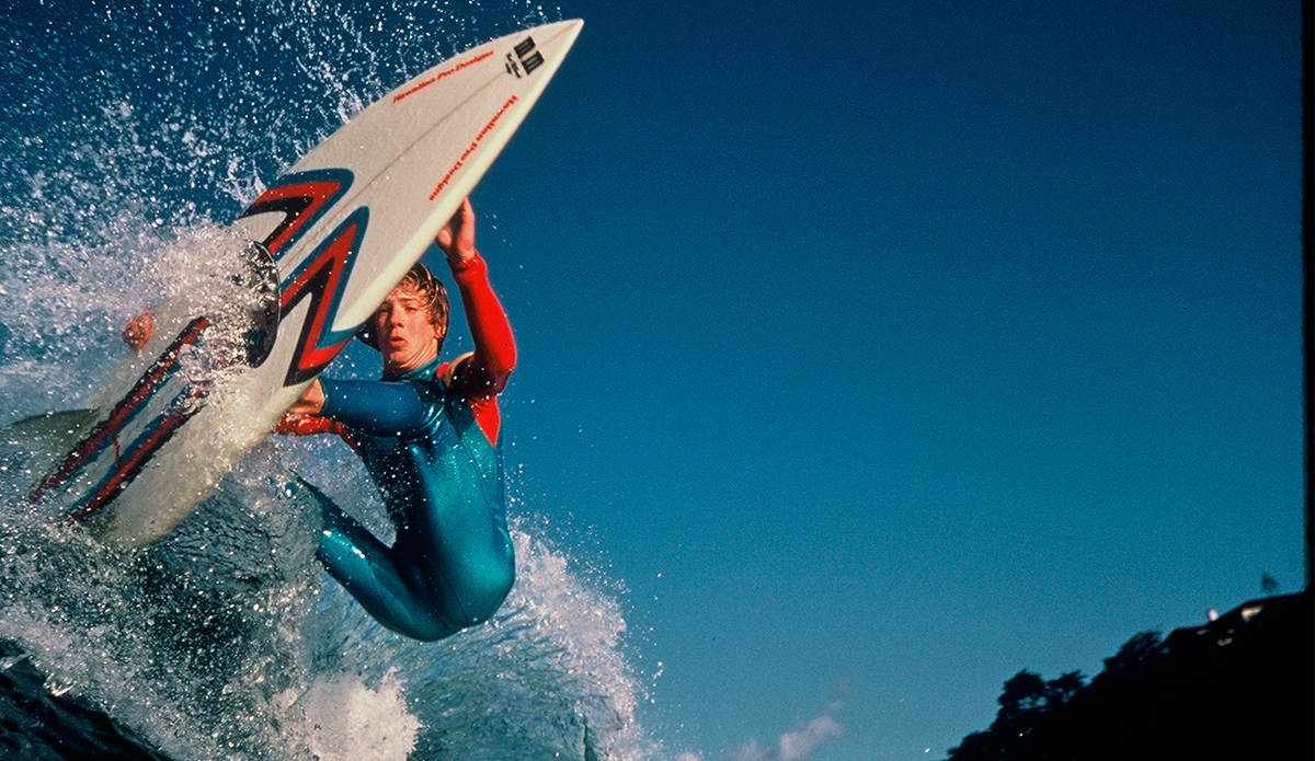 Mark has been shredding for 42 years now! He started  surfing at age 8.  A few cool locals David, Jack, and Buttons helped him get involved and showed him how to place a surfboard in the sand to practice standing up. This photo was his first cover shot for a local magazine called BREAKOUT. He\'s riding a DT surfboard and wearing a classic Victory wetsuit. Photo by: Chuck Gomery.