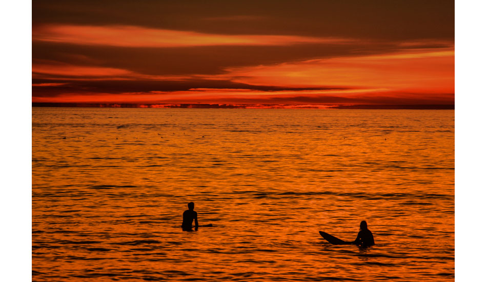 2 surfers floating in orange reflections. Ocean Beach, San Diego.