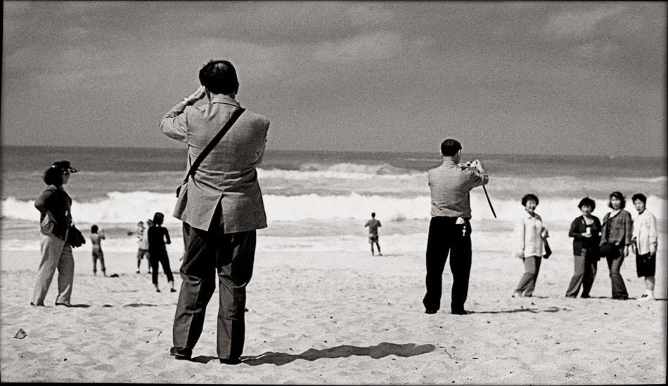 If you\'ve been to Sunset Beach you will have seen this scene. The tourists jump off the buses, get their pix, and jump back in. I\'ve watched it time and time again - I love it. Here a surfer in the background looks a little deeper into the world before him. Photo: <a href=\"http://www.submerge.com.au\" target=_blank>Dean Dampney</a>.