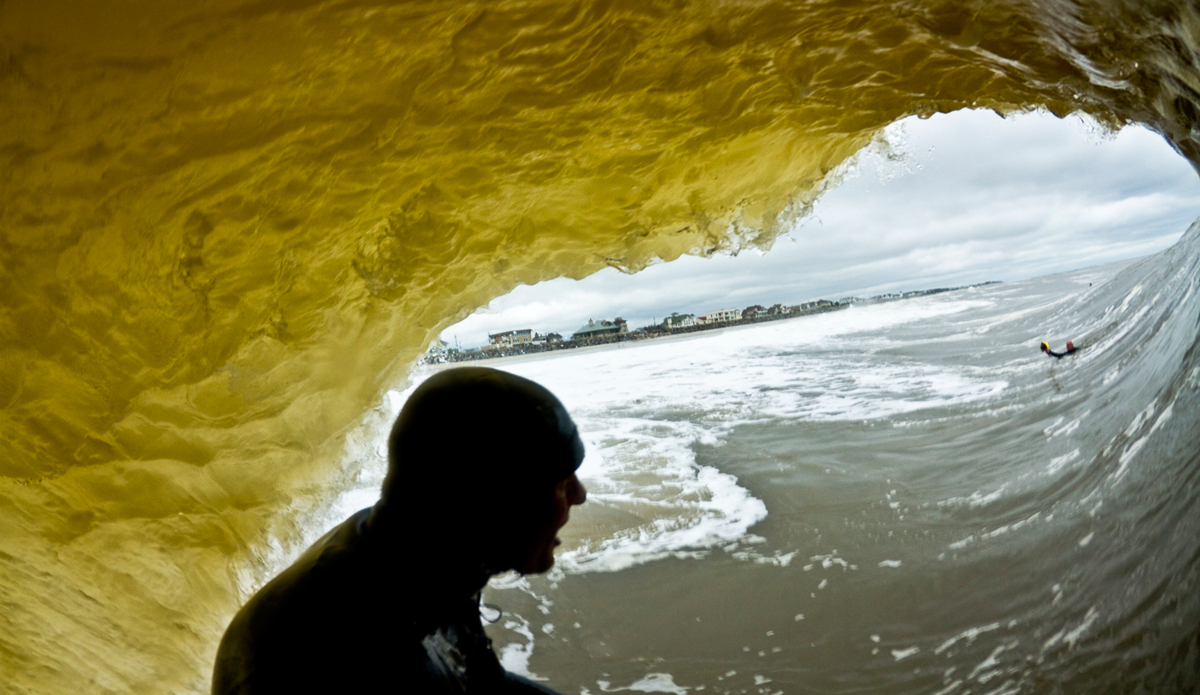 Kind of an ironic image and a similar one to the one Seth Stafford shot a few years back, although Seth\'s photo bests this one ten-fold. The sand had just been pumped in Monmouth County and it created this nuts sand bank with a ripping current. I was shooting from the beach for a while, as were a ton of other photographers (insert bitter Jersey attitude here). I couldn\'t seem to find my own angle. Rippers started showing up in droves, Mike and Sam were still getting the best waves of the day and I was yet to make an image I was happy with. A bit frustrated I threw the Hail Mary and put my fisheye into the Essex Housing. I walked up the beach, jumped in and swung into position a number of times, never holding my ground for more than a few minutes. On one of my last attempts I saw Sam go for one and I followed him through the wave for this perspective shot. As you can see, I still couldn\'t get away from the photographers this day, it was that good. Photo: <a href=\"http://www.ryanstruck.com/\"> Ryan Struck</a>