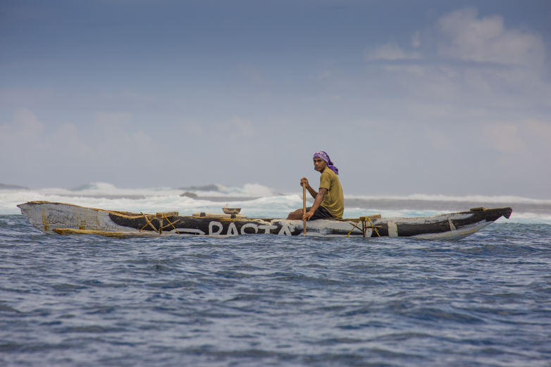 Locals in dugout canoes ride the swell while divers are in the water collecting various fish and edibles. In an hand-to-mouth economy, the ocean provides much of the island with food.
