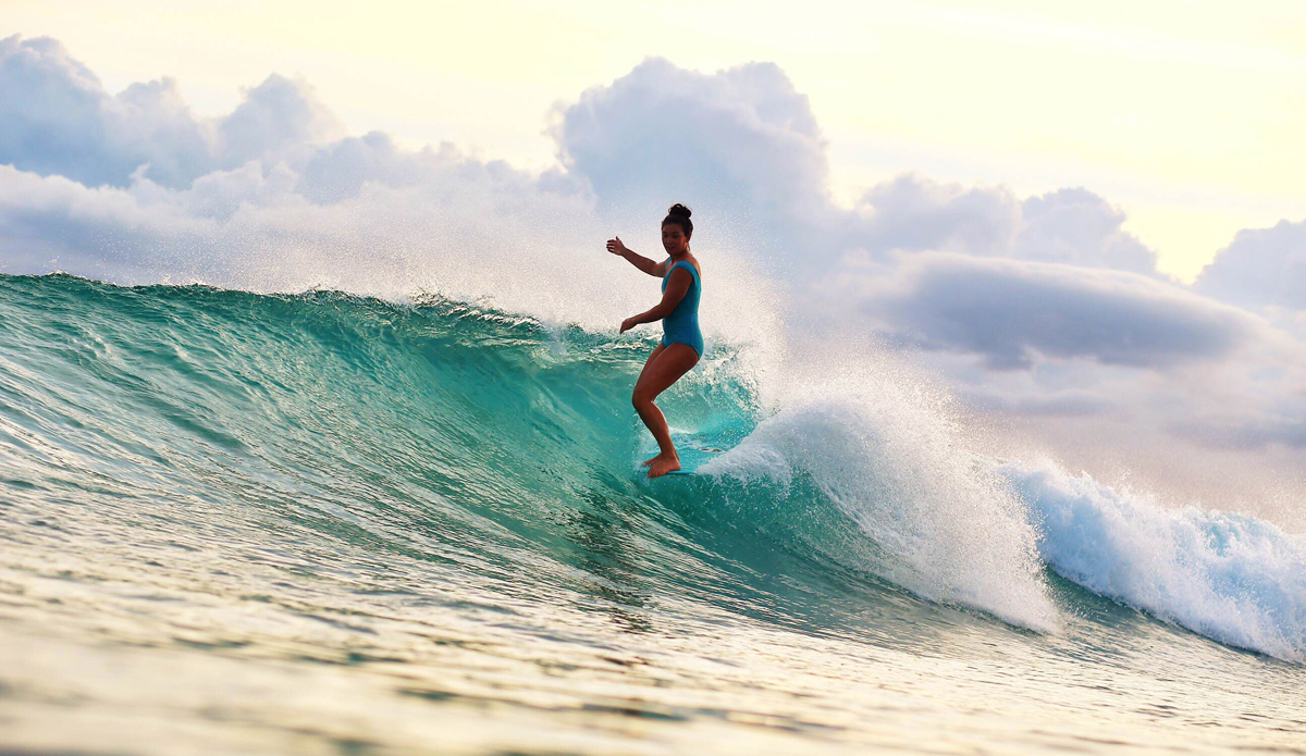 Rosie Jaffurs (@rosiejaffurs) is born and raised on the North Shore of Hawaii. Most would never guess that the mecca for big waves and carnage would foster an environment for traditional longboarding. I first met Rosie one early morning on the North Shore. She was on a single
fin log and got barreled right in front of me. As a California transplant who hides out at point breaks, this blew my mind. So, naturally, I cornered her in the water and demanded we should be friends. I found out quickly that Rosie and her boyfriend Keoki were apart of the
traditional longboard movement in Hawai\'i and that they were both world-class surfers. They took me under their wing and showed me what it means to surf with aloha. Rosie nose-riding in a critical section. Photo: Keoki Saguibo (@photokeoki)