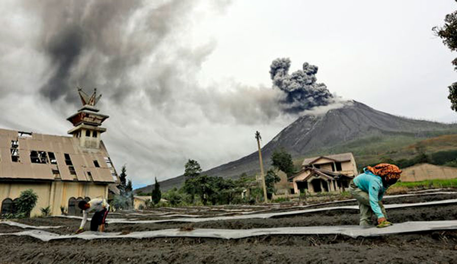 Villagers work at their farm as Mount Sinabung spews volcanic materials during an eruption, in Karo, North Sumatra, Indonesia