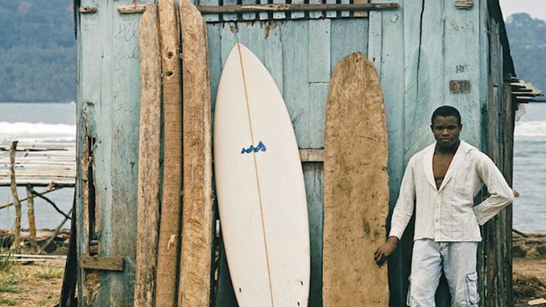 A surfer stands next to traditional boards in africa