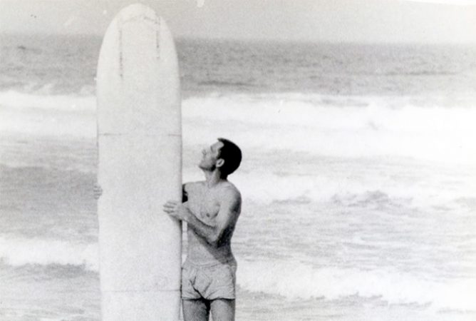 Nikolai Petrovich Popov with his surfboard in front of the ocean