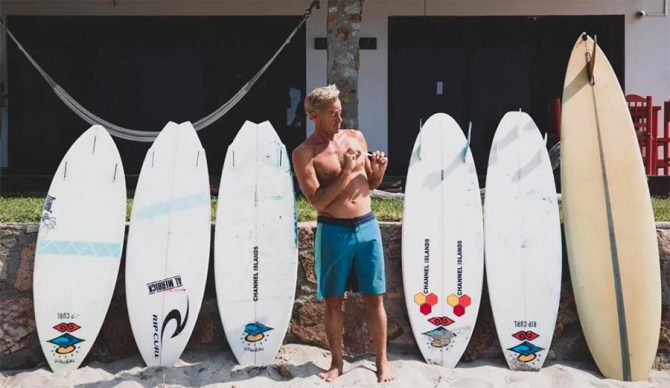 Tom Curren stands in front of his surfboard quiver