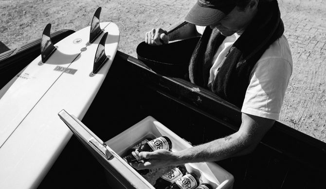 a surfer grabs a beer from the back of his truck