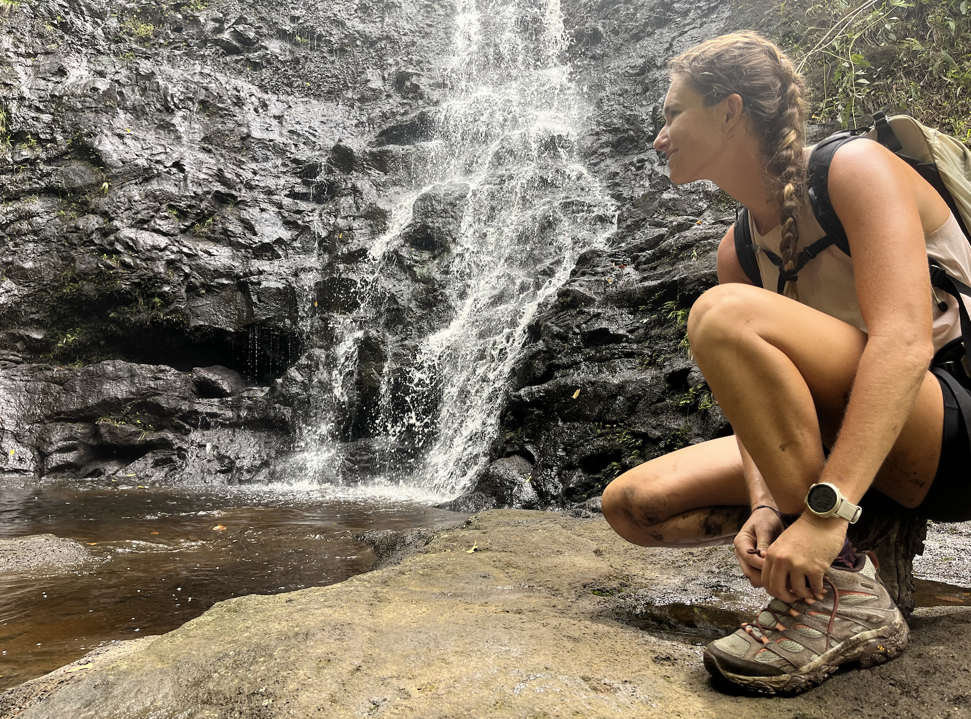 a woman tying her hiking boots in front of a waterfall