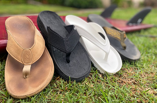 four different men's sandals lined up against a surfboard.