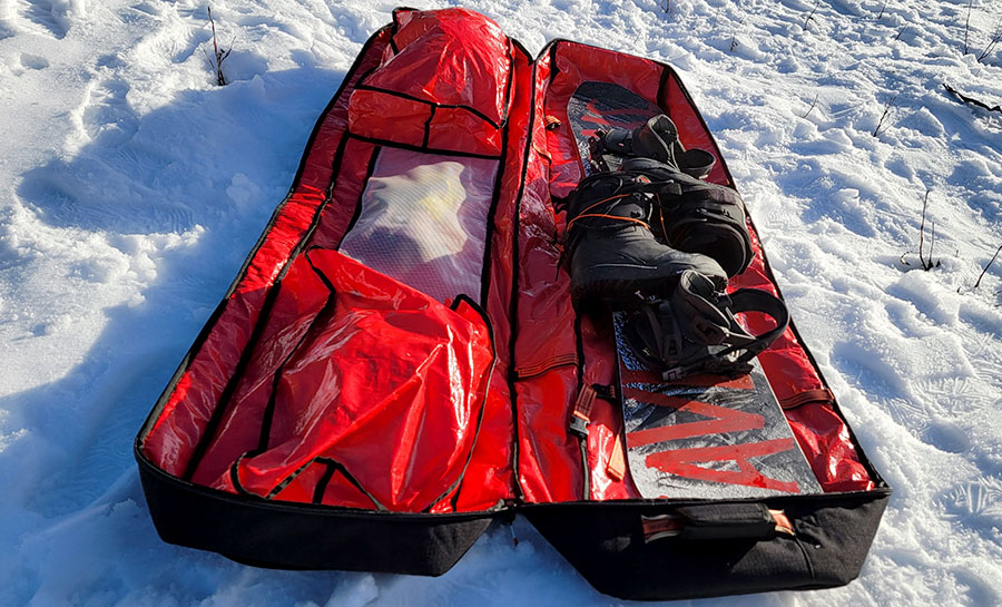 The Season snow roller bag with snowboarding gear inside, laying on the snow