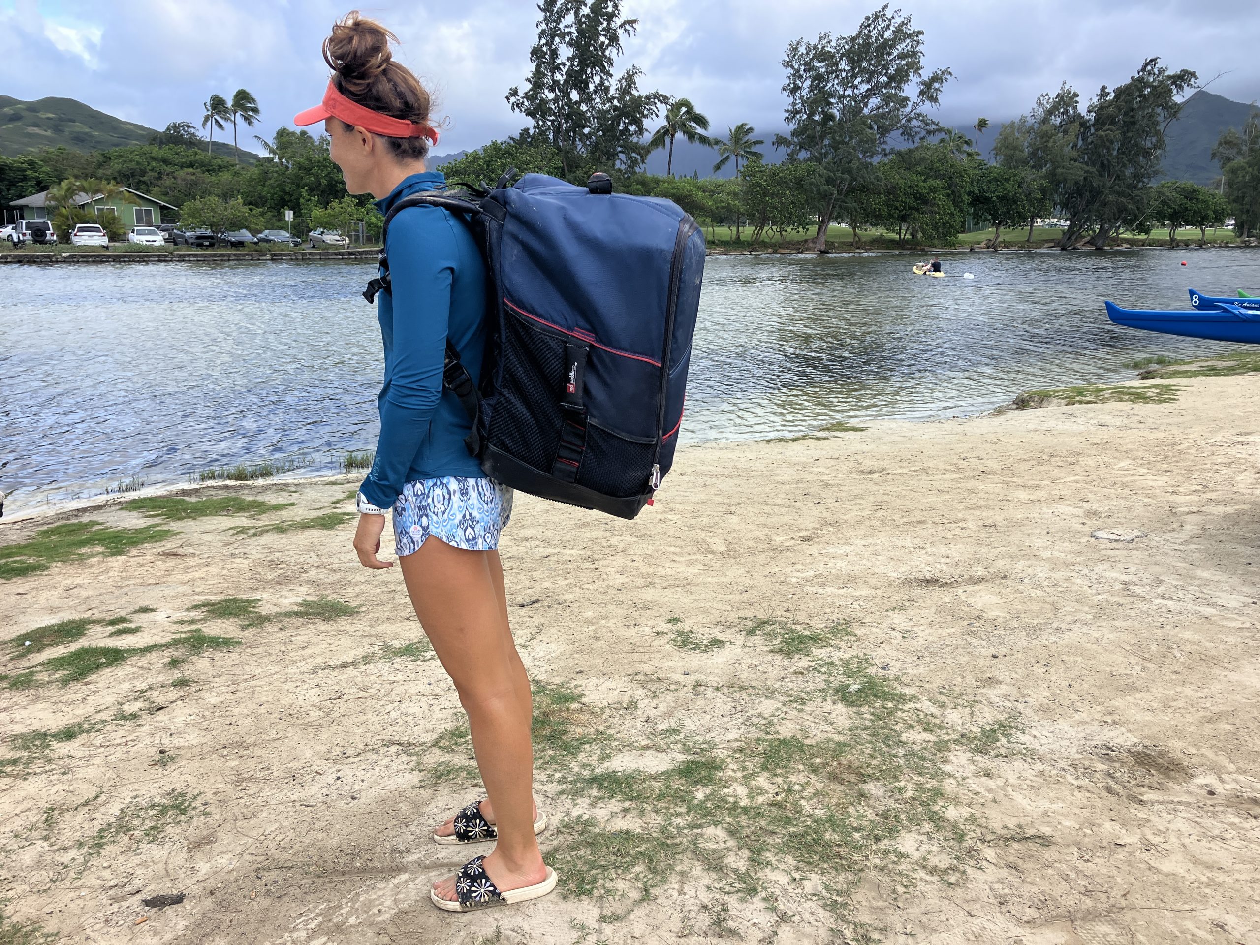 woman standing on the beach with an inflatable paddle board in a backpac