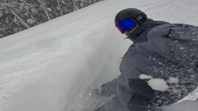 a snowboarder makes a slash in powder while testing the trew gear jacket and bibs