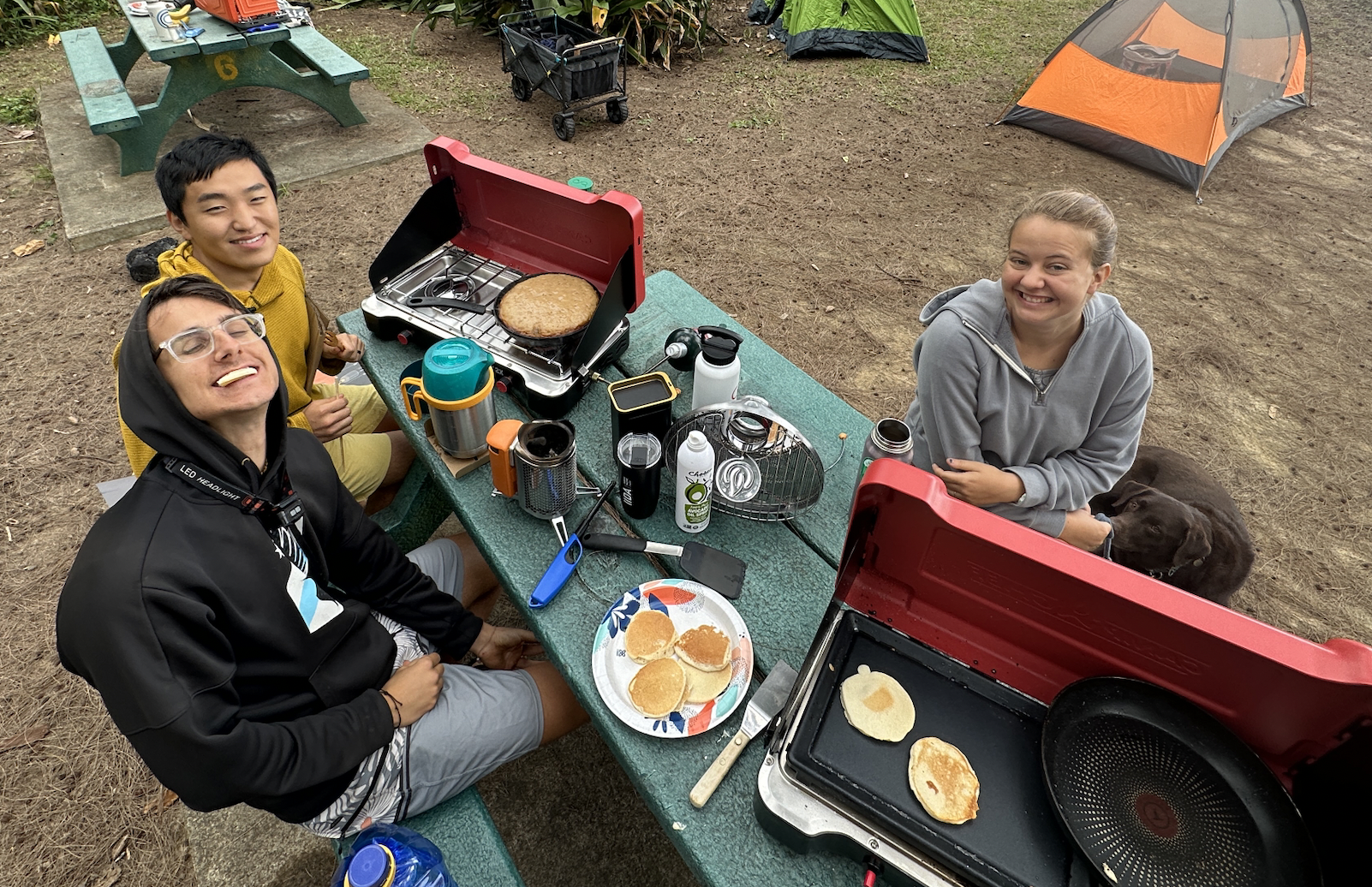 some people sitting around camping stoves at a campsite