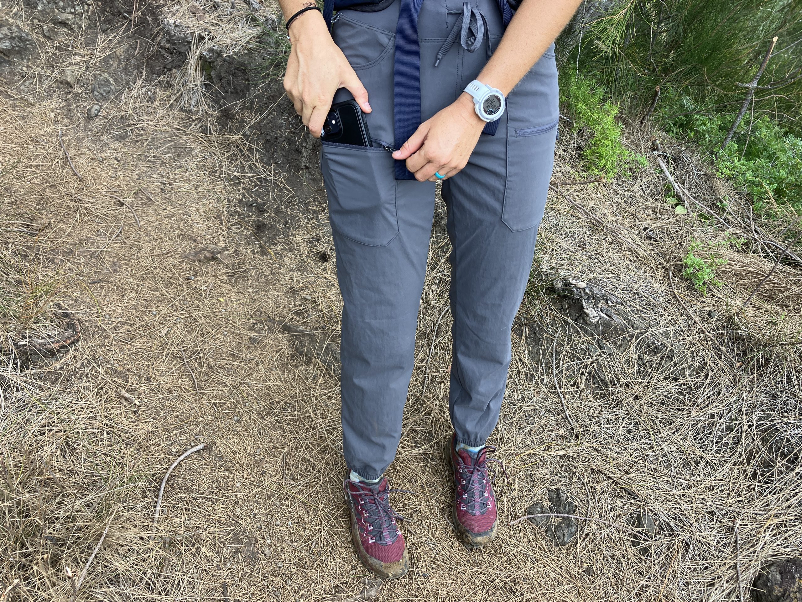 a close up of someone putting a phone in the pocket of hiking pants