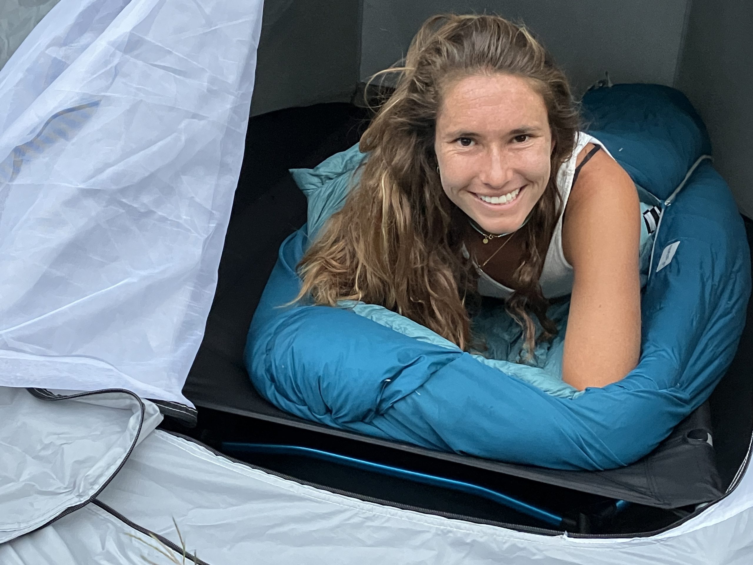 a woman sleeping on a camping cot in a sleeping bag