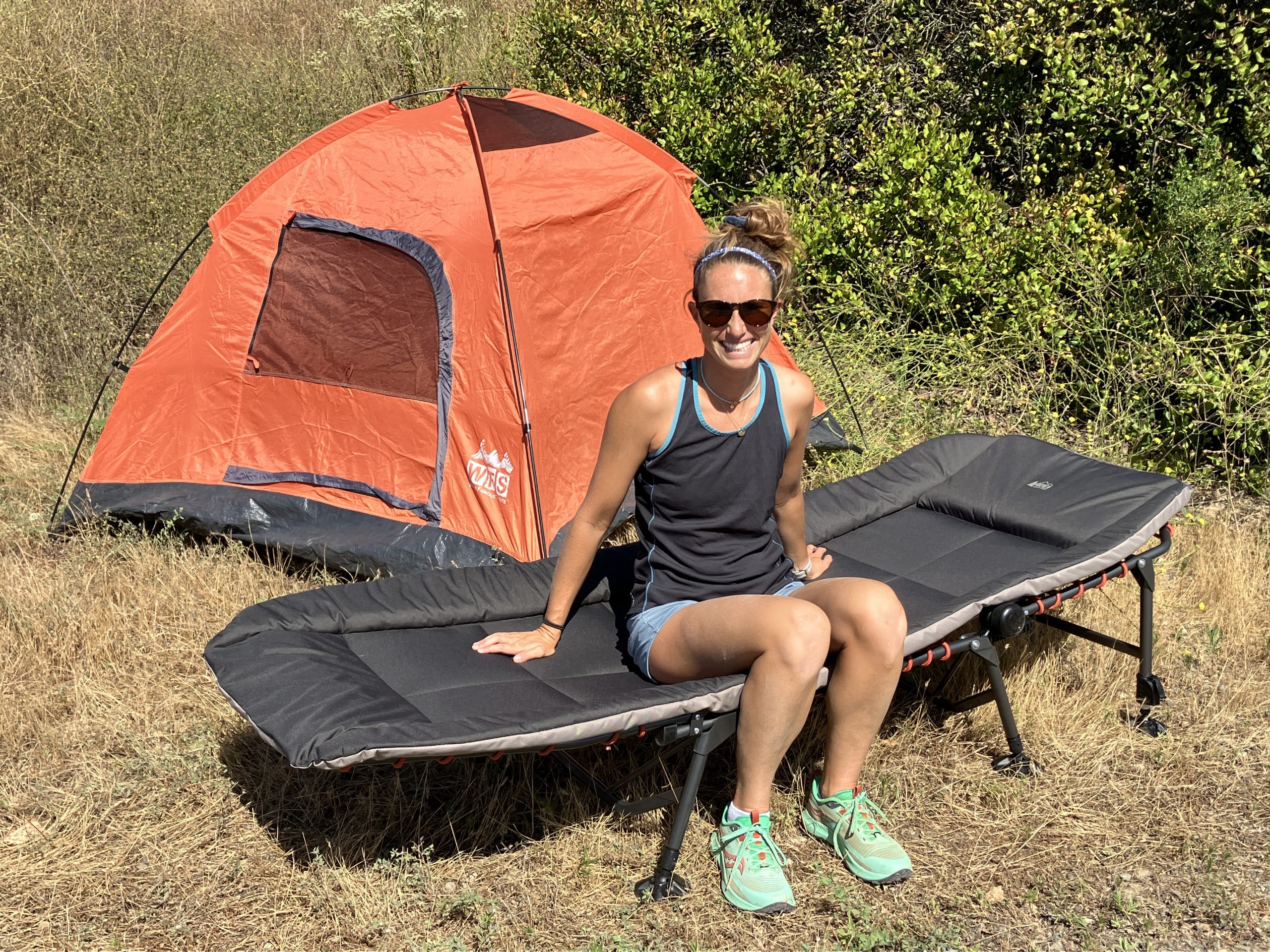 a woman sitting on a camping cot in front of a tent