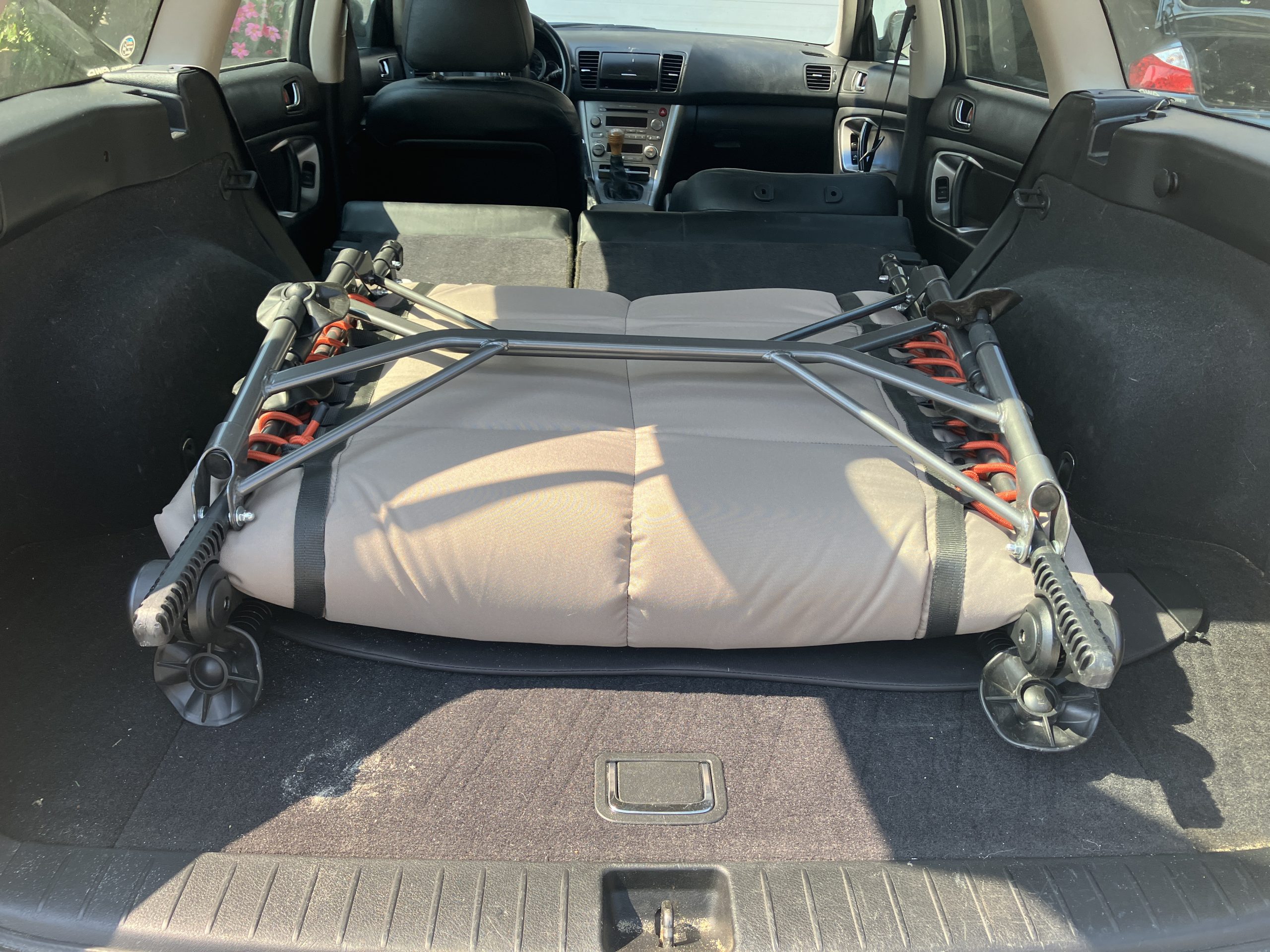 a camping cot folded up and in the trunk of a car