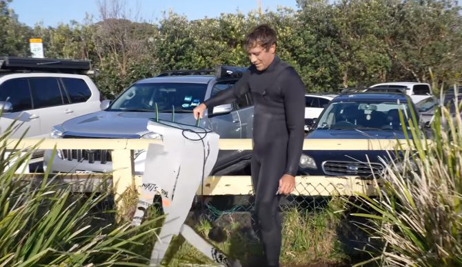 Koa Rothman holding the flayed remains of his surfboard. Photo: Koa Rothman // YouTube