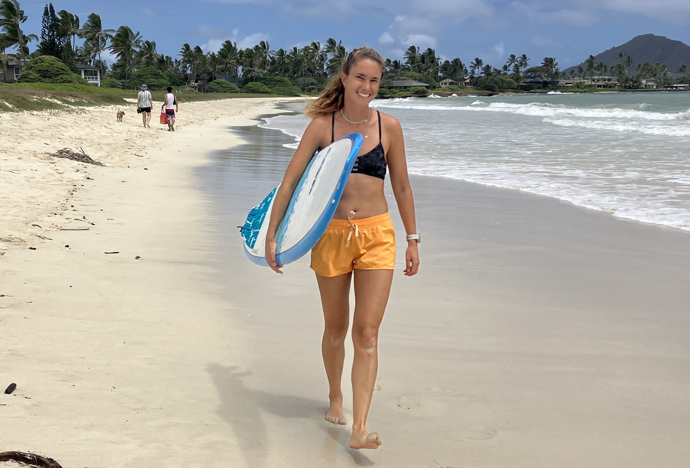 a woman walking down the beach carrying a surfboard 