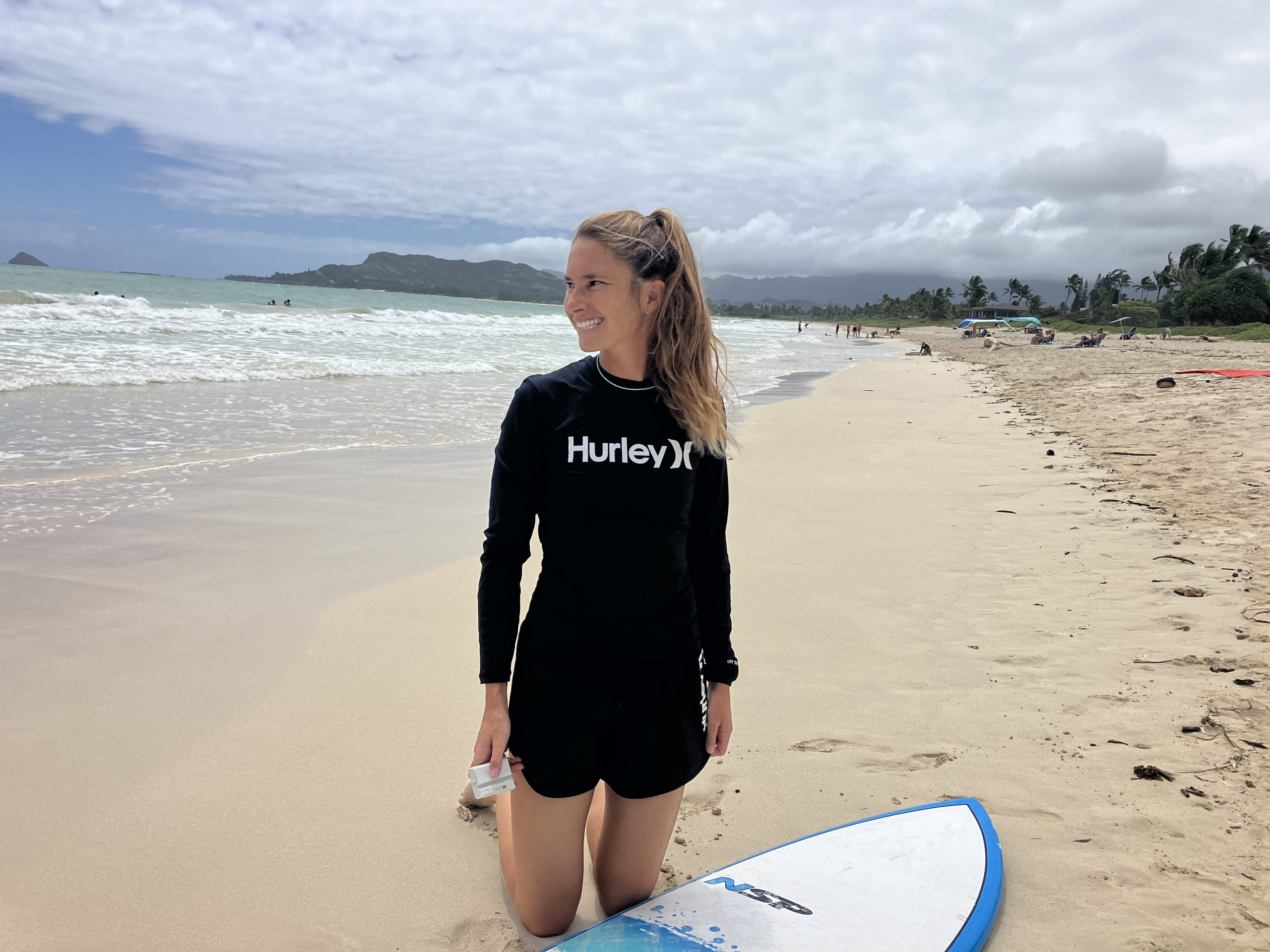 a woman kneeling on the beach next to a surfboard