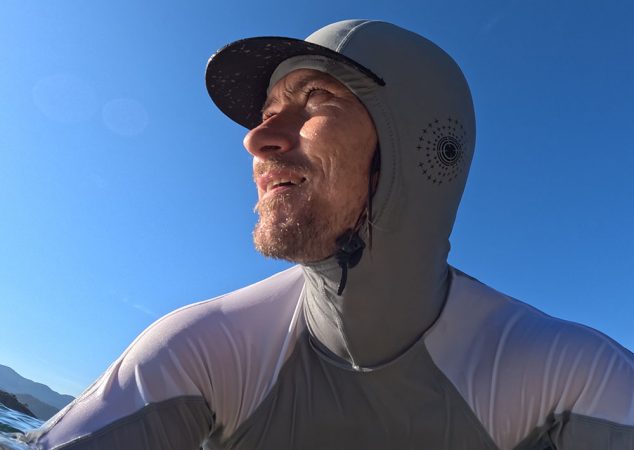 a surfer looks out to the ocean with a hooded rash guard