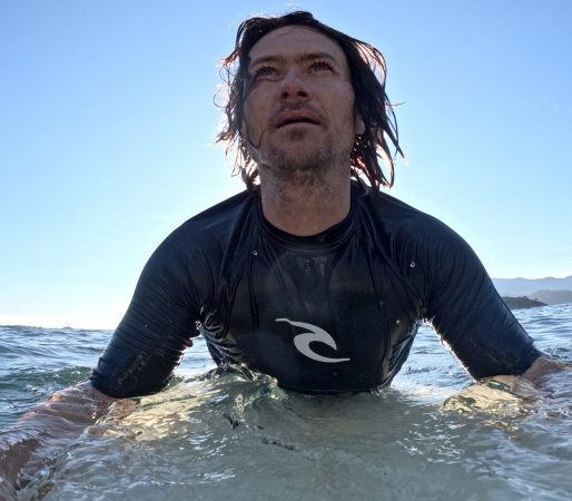 a surfer looks for waves while sitting on his surfboard, wearing a rash guard