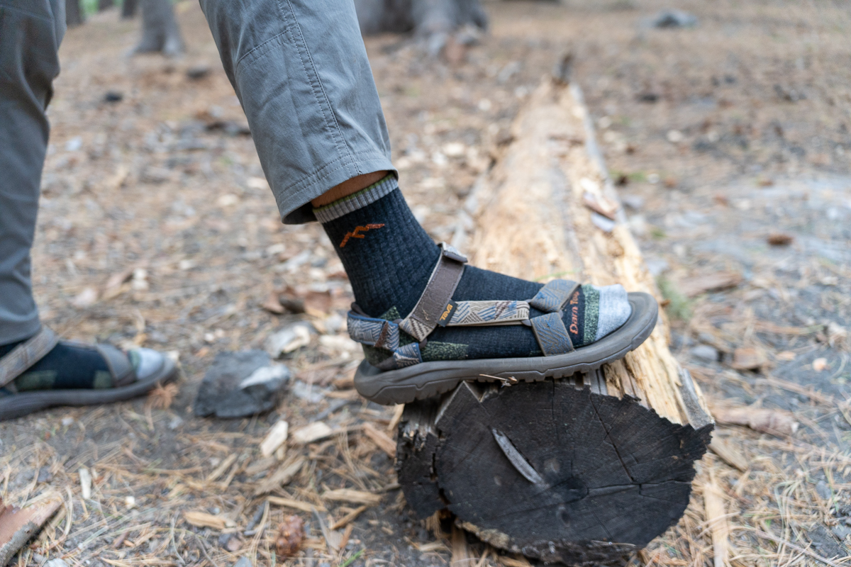 man stepping on log in hiking sandals and socks