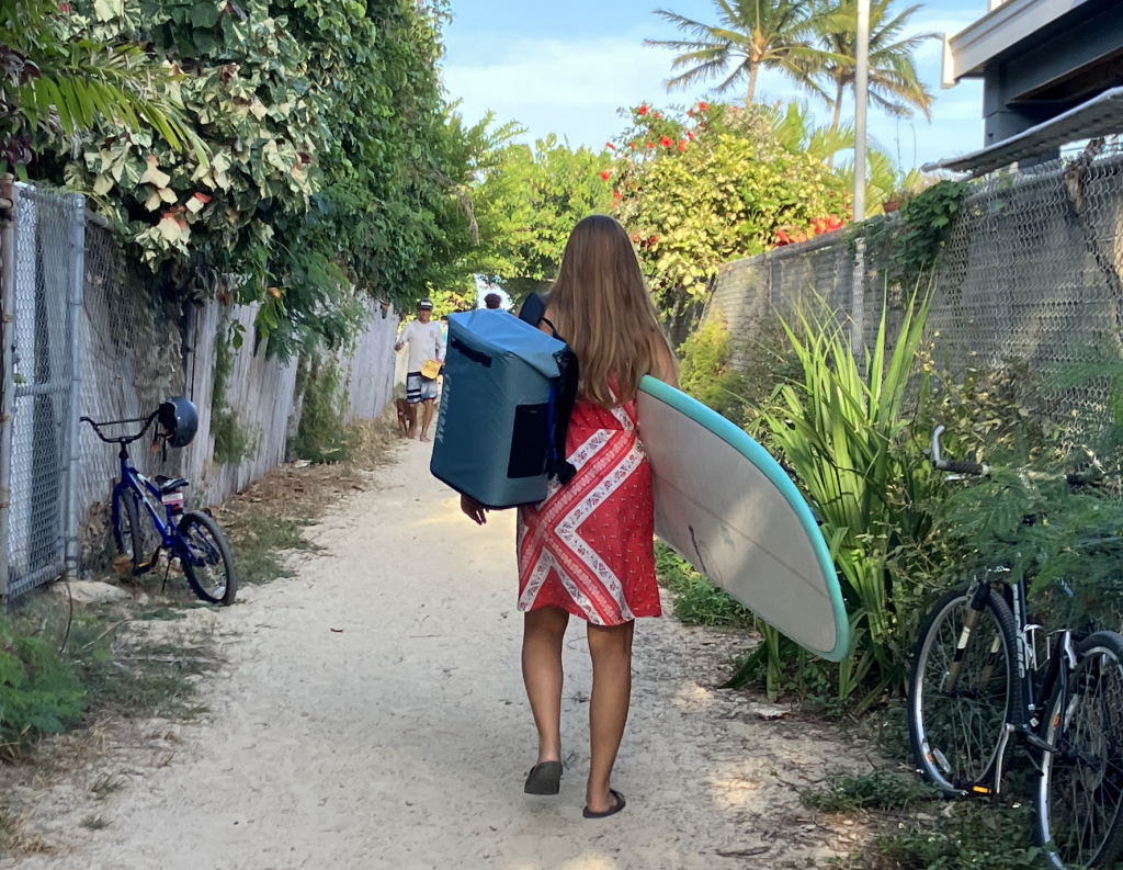 woman carrying backpack cooler and surfboard