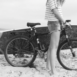 Woman standing with a surfboard on a bike rack at the beach