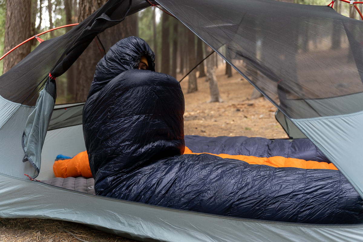 man sitting in a backpacking sleeping bag with head in hood