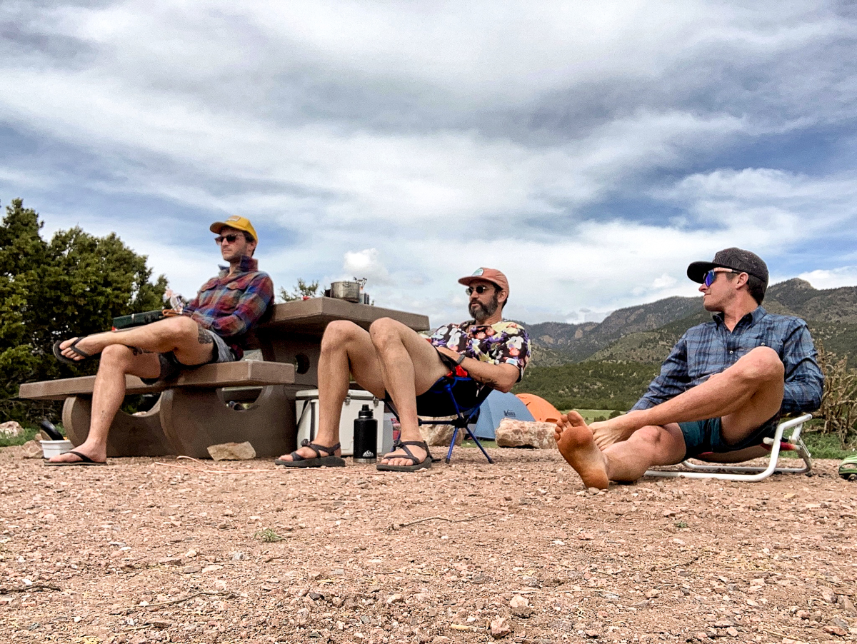 three men sitting at camp in sun shirts